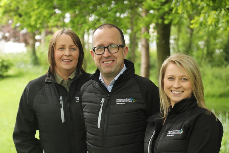 3 smiling people surrounded by trees