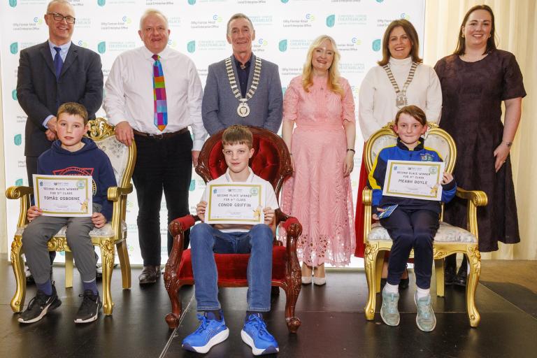 Children sitting with awards and adults standing
