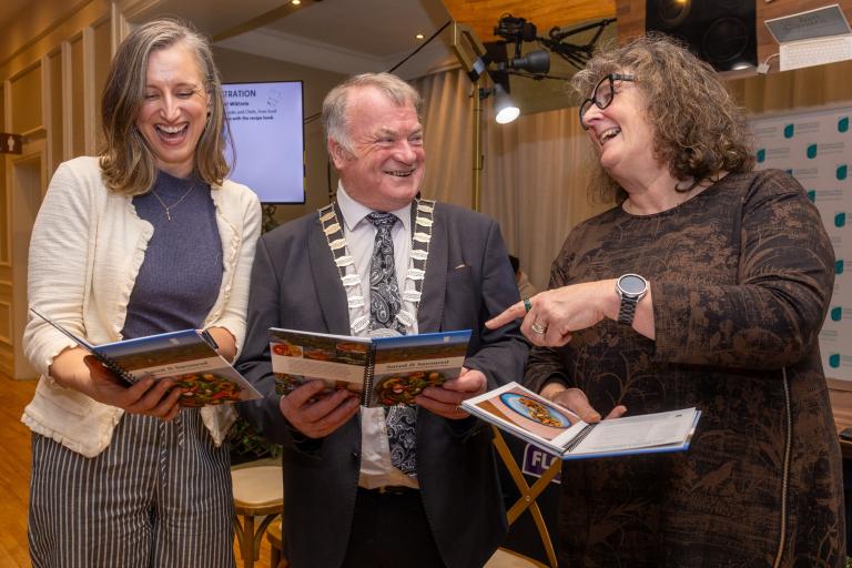 3 people looking at a book and smiling