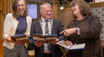 3 people looking at a book and smiling